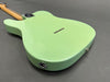 Back view of a pastel green solid body electric guitar with a bolt-on maple neck and six string ferrules on a gray background