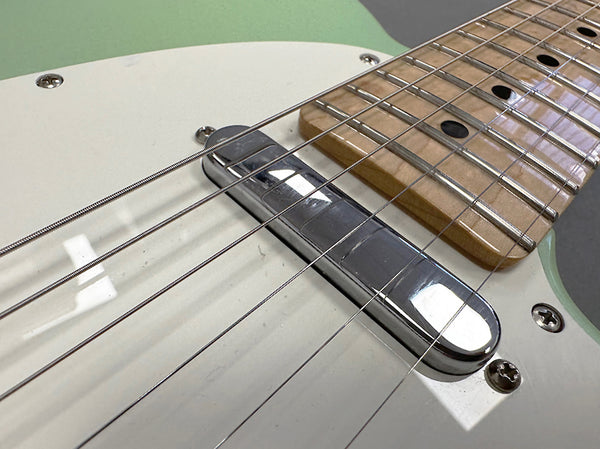 Close-up of electric guitar bridge and pickup with maple fretboard and white pickguard on a green body guitar