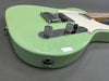 Close-up of seafoam green electric guitar body with chrome control knobs and bridge on gray background