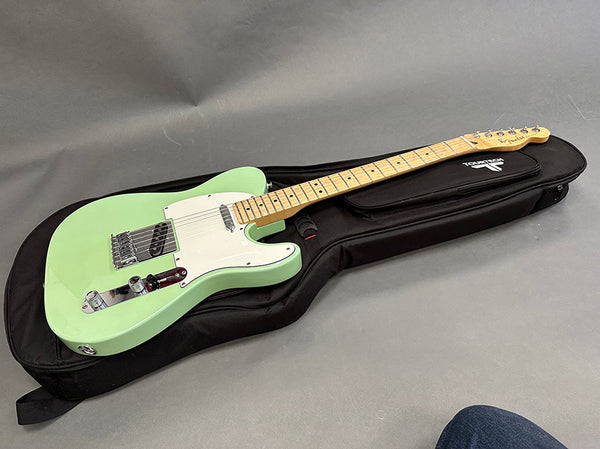 Seafoam green Fender Telecaster electric guitar with maple neck and white pickguard resting on black soft guitar case on gray background