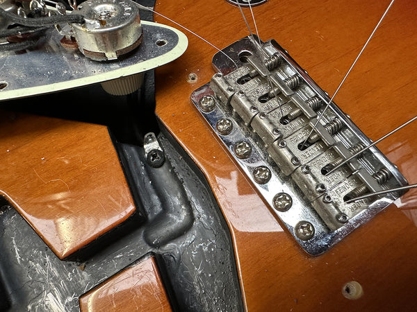 Close-up of vintage electric guitar body showing chrome Fender bridge with strings and open cavity for pickups and electronics on a honey burst finish guitar