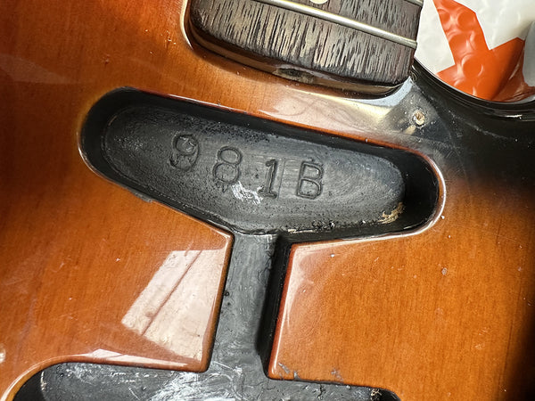 Close-up of guitar body cavity showing serial number 981B stamped inside with sunburst finish and wood grain visible near pickups