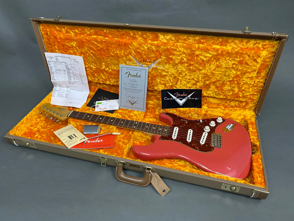 Vintage pink Fender electric guitar with rosewood fretboard inside a hardshell case with bright orange plush interior, including Fender certificate of authenticity, owner's manual, and maintenance receipt.