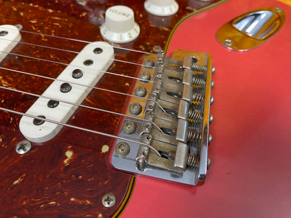 Close-up of red electric guitar bridge, white single-coil pickups, and volume knobs with tortoise shell pickguard screws visible