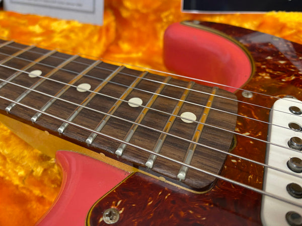 Close-up view of electric guitar fretboard with worn orange and red body in a yellow plush case