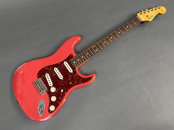 Vintage Fender Stratocaster electric guitar in worn red finish with tortoiseshell pickguard and rosewood fretboard on gray background