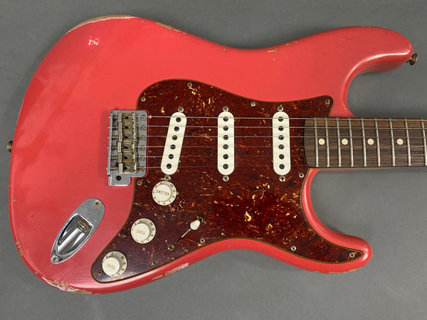 Vintage red electric guitar with tortoiseshell pickguard and three single-coil pickups, featuring volume and tone control knobs and chrome hardware, showing signs of wear and aging.
