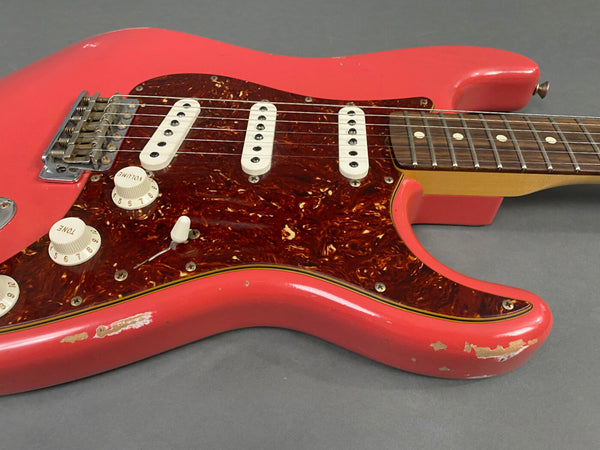 Close-up of vintage red electric guitar body with tortoiseshell pickguard, three single-coil pickups, volume and tone knobs, and maple neck on gray background