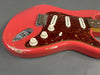 Close-up of vintage red electric guitar body with tortoiseshell pickguard, three single-coil pickups, volume and tone knobs, and visible wear and scratches on the finish