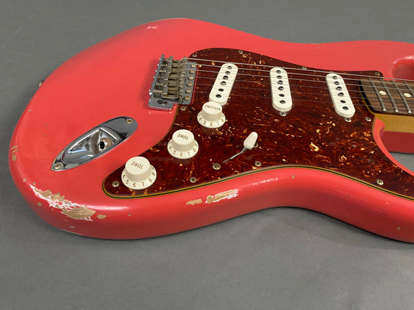 Close-up of vintage red electric guitar body with tortoiseshell pickguard, three single-coil pickups, volume and tone knobs, and visible wear and scratches on the finish