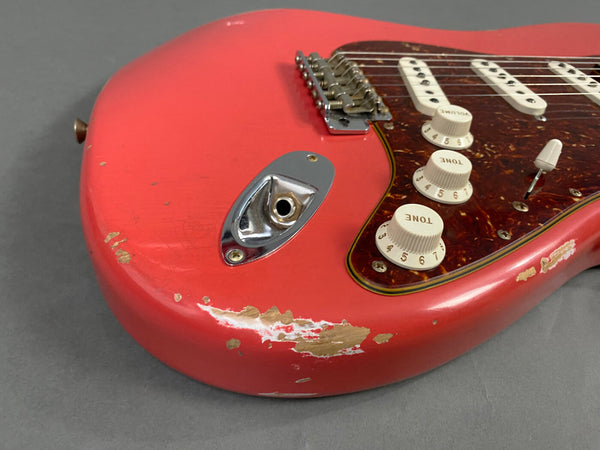 Close-up of red electric guitar body with worn paint, white tone and volume knobs, tortoiseshell pickguard, and chrome input jack plate on gray background