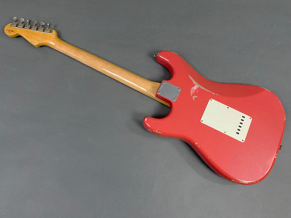 Rear view of a red electric guitar with visible wear and wood neck, showcasing the back plate and tuning pegs on a gray background.