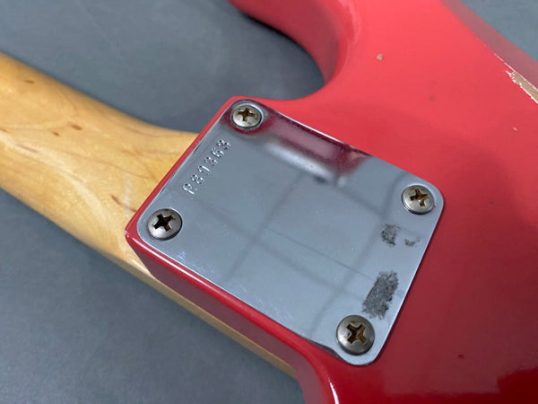 Close-up of red electric guitar neck joint plate with serial number P890363 and four screws on natural wood neck and red guitar body