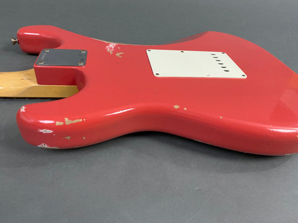 Close-up of worn red electric guitar body with white backplate and maple neck on gray surface