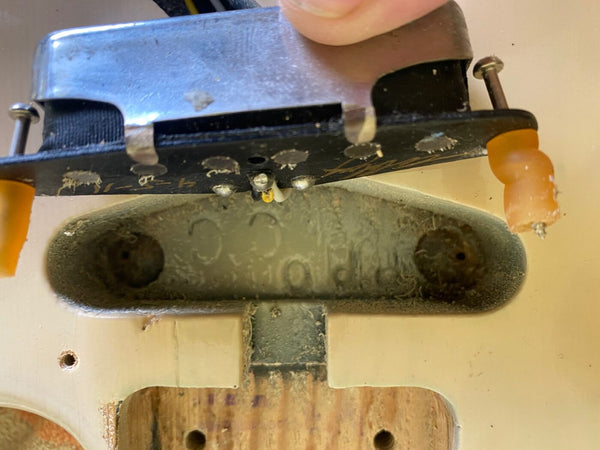 Close-up of vintage electric guitar single-coil pickup being removed from the pickup cavity showing aged pickup cover, screws, and worn guitar body wood.