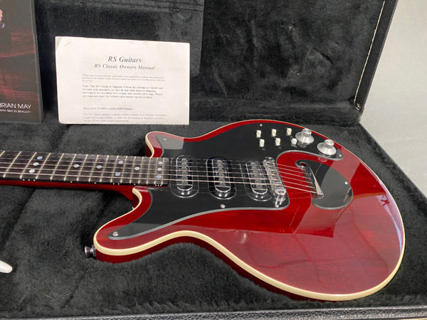 Red RS Classic electric guitar with black pickguard, triple single-coil pickups, and control knobs, displayed in a black plush-lined hard case with RS Guitars owner's manual.