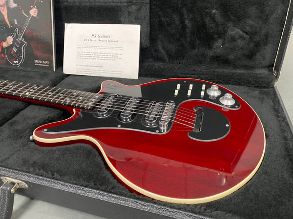 Red RS Classic electric guitar with black pickguard and multiple control knobs in a black plush guitar case with owner's manual and Brian May book in the background