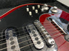 Close-up of electric guitar bridge and pickups showing Burns Tri-Sonic chrome pickups and string saddle on red and black guitar body with control knobs