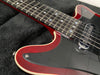 Close-up of red electric guitar body and neck with black pickguard and metal strings on black fabric background