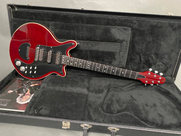 Red electric guitar with black pickguard and three pickups inside a black plush-lined hard case with brochure beneath guitar body