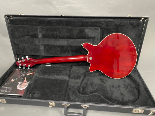 Back view of red electric guitar inside black hard case with plush interior and Brian May red special booklet