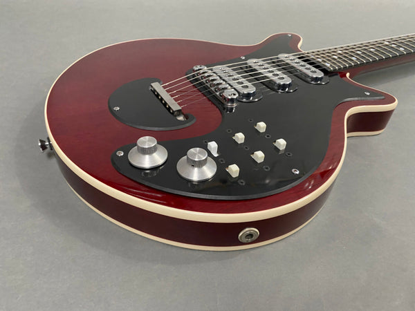 Close-up of red electric guitar body with black pickguard, chrome pickups, multiple white switches, and silver control knobs on gray background