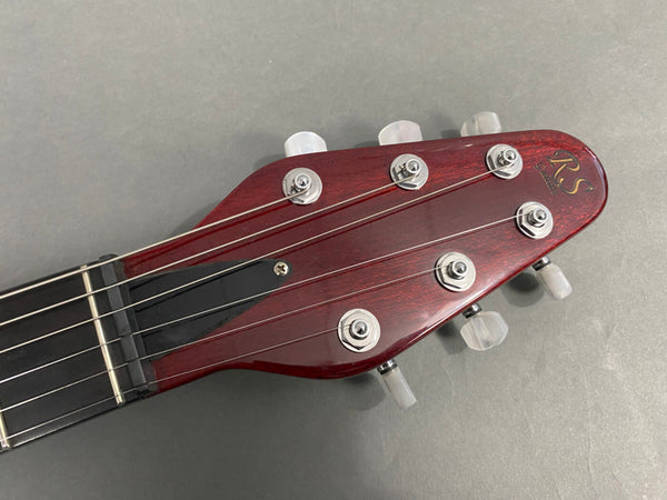 Close-up of RS Guitars red wooden electric guitar headstock with six tuning pegs and strings on gray background