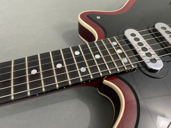 Close-up view of electric guitar neck with dot inlays and metal frets, showing black body with dual chrome pickups and cream binding on red edges.