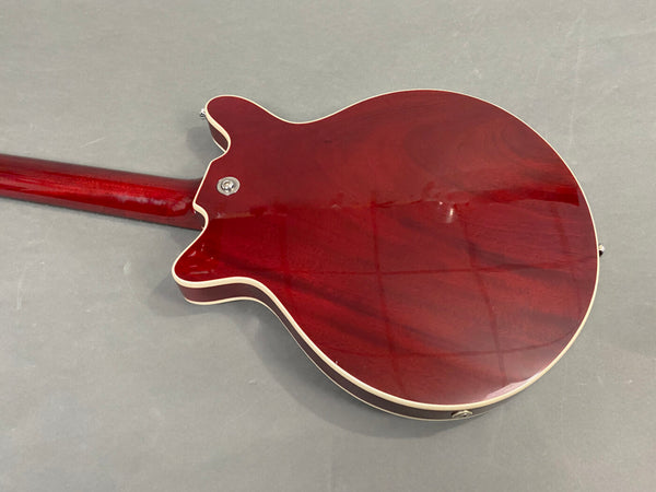 Back view of a cherry red semi-hollow electric guitar with cream binding on body and neck, displayed on a gray surface.