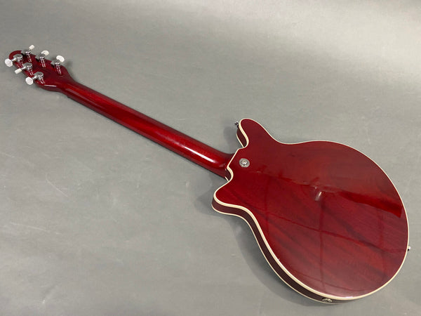 Back view of red electric guitar with glossy finish and cream binding on body and neck, showing tuning pegs and strap buttons on gray background.
