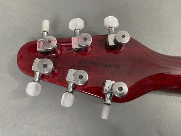 Back of red guitar headstock showing chrome Grover tuning machines and serial number RS2004106-54 on gray background
