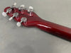 Close-up of the back of a red guitar headstock with six chrome tuning pegs and serial number visible, displayed on a gray surface.