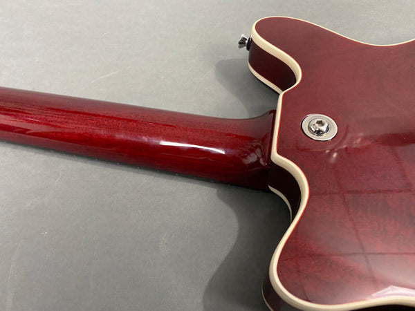 Close-up of cherry red electric guitar neck joint with cream binding and strap button on gray background