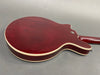 Back of dark red electric guitar with cream binding and strap button on gray background
