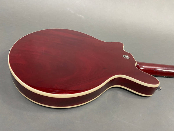 Back of dark red electric guitar with cream binding and strap button on gray background