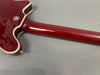 Close-up of glossy red electric guitar neck and body joint with cream binding and strap button on gray surface