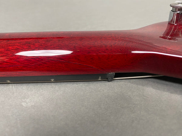 Close-up of a red electric guitar neck showing a visible crack in the wood near the fretboard edge and tuning peg.