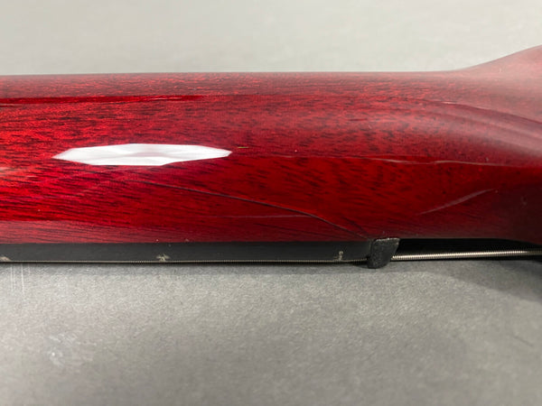 Close-up of a red guitar neck showing wood grain and a visible crack near the guitar string on a gray surface