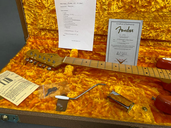 Fender Stratocaster guitar neck inside vintage orange plush-lined guitar case with Certificate of Authenticity, maintenance checklist, tremolo arm, and instructional pamphlet from Coffee House Guitars.