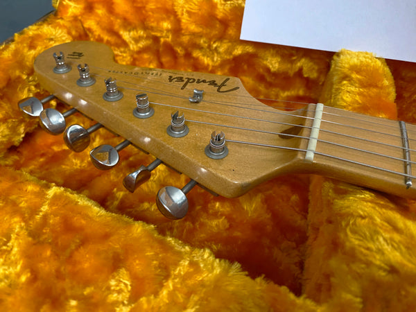 Close-up of Fender electric guitar headstock with six tuning pegs, resting on bright orange plush guitar case lining