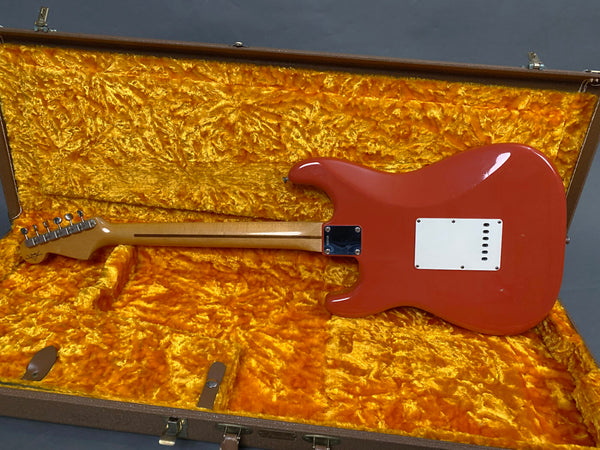 Back view of red electric guitar with maple neck in open vintage orange plush-lined hard case on gray background