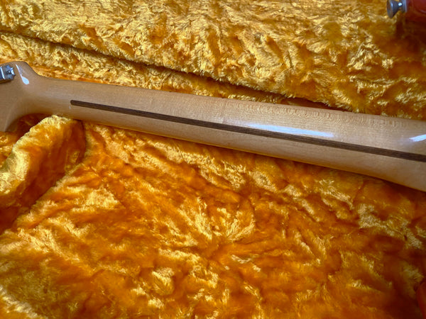 Maple guitar neck with skunk stripe detail resting on a plush orange guitar case lining