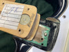 Close-up image of the neck pocket of an electric guitar showing neck heel with handwritten notes, mounting screw, and part of the black and white guitar body with visible wear and green paint inside the neck cavity.