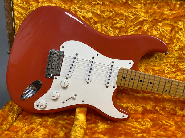 Red electric guitar with white pickguard and three single-coil pickups resting on a plush yellow guitar case lining