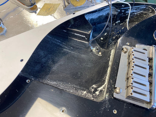 Close-up of black electric guitar body showing pickup cavity and tremolo bridge with worn and dusty finish, guitar wiring exposed, from Coffee House Guitars product listing.