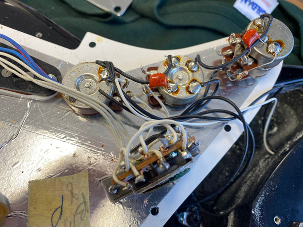 Close-up image of electric guitar internal wiring and potentiometers with capacitors and soldered connections for pickup selector and volume controls.