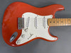 Electric guitar with orange body, white pickguard, maple neck, and three single-coil pickups on gray background