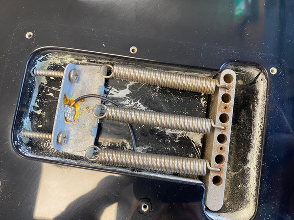 Close-up of vintage guitar tremolo springs and claw inside black guitar body cavity showing metal plate, screws, and wiring details for electric guitar bridge system.
