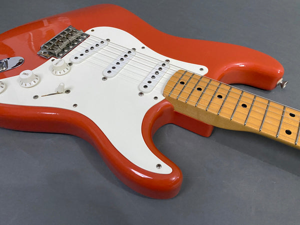 Close-up of a red electric guitar with white pickguard, maple neck, single-coil pickups, and tone and volume control knobs on a gray background