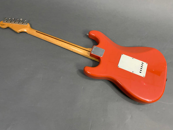 Rear view of a red electric guitar with a maple neck and metal tuning pegs on gray background